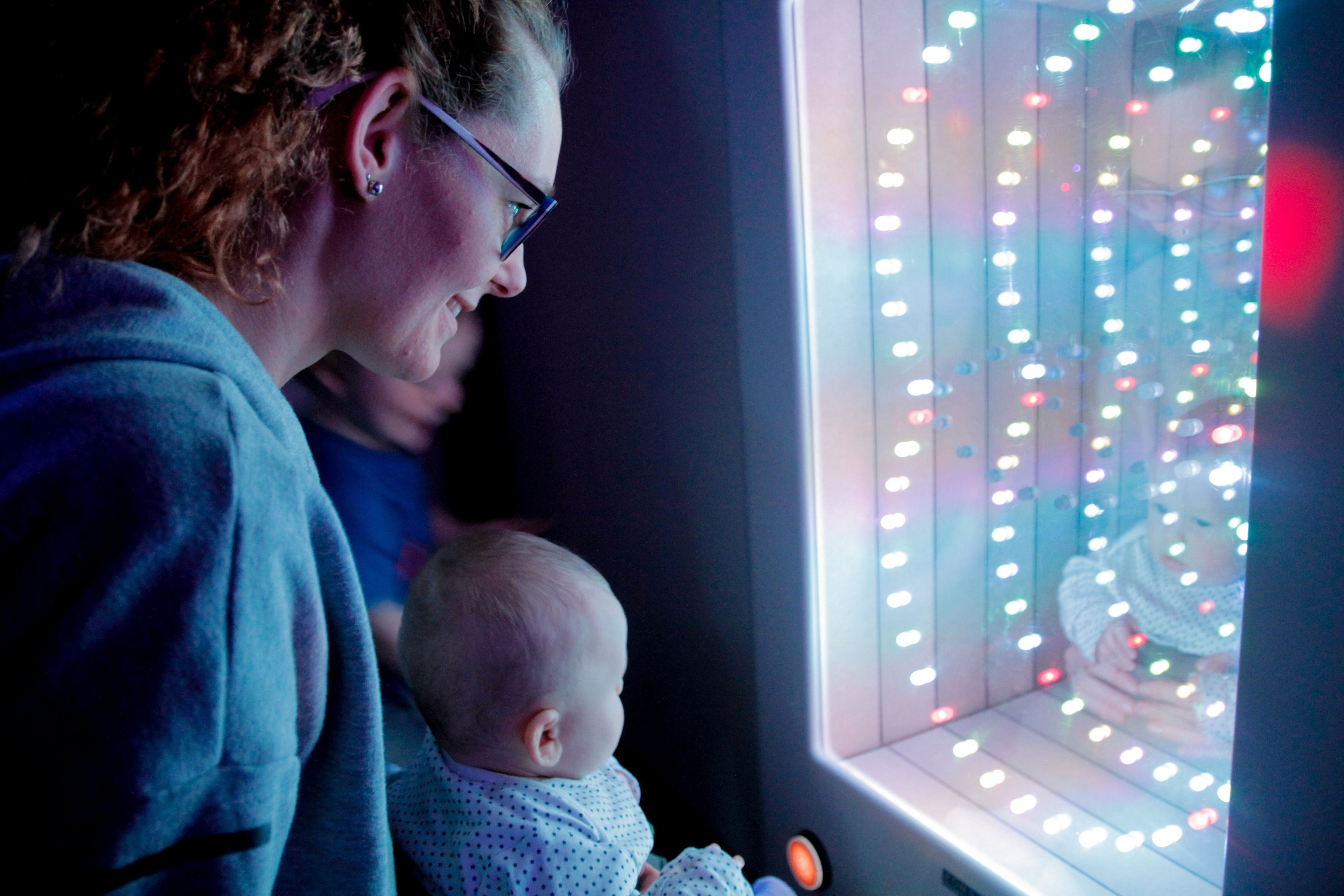 Iemand houdt een baby vast voor een raam met decoratieve verlichting.