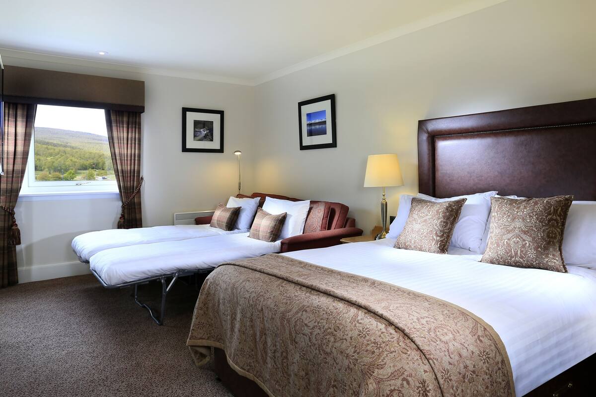 A hotel room with two beds, a large window with curtains, a headboard, and a lamp.