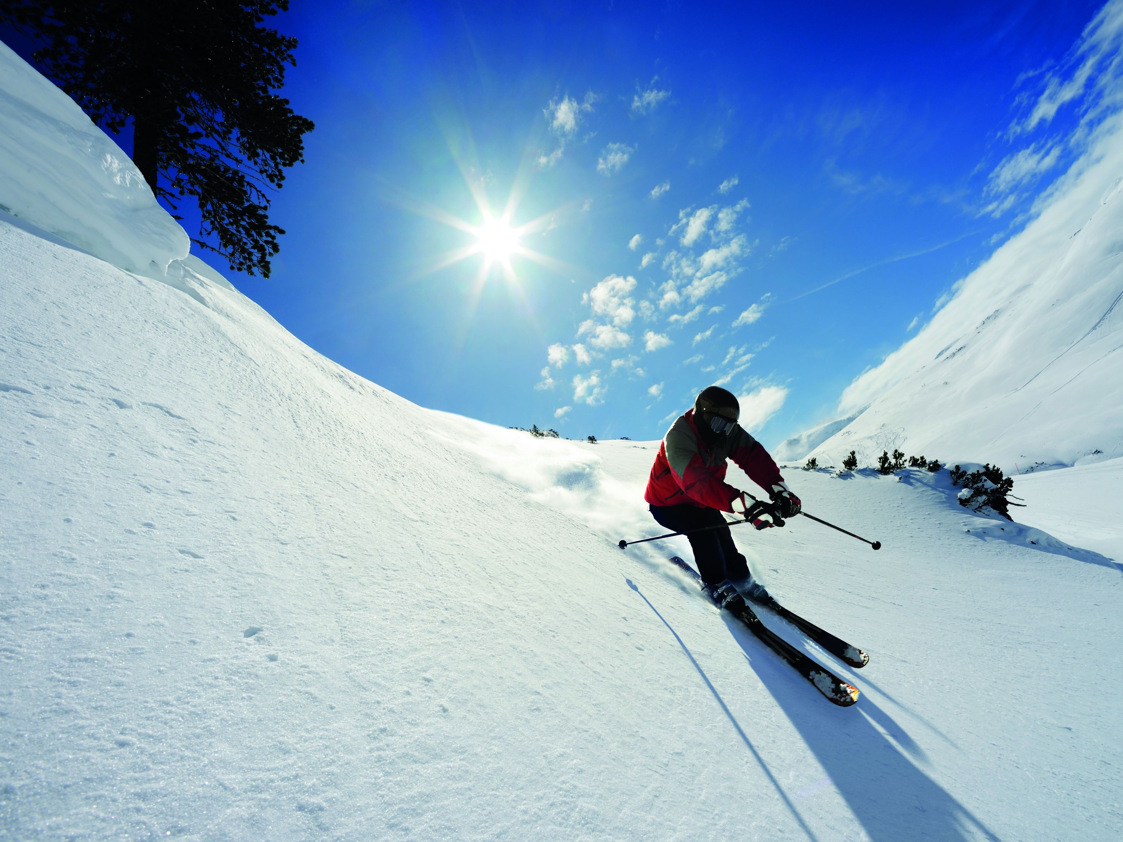 A person skiing down a snowy slope with a clear sky and sun shining.