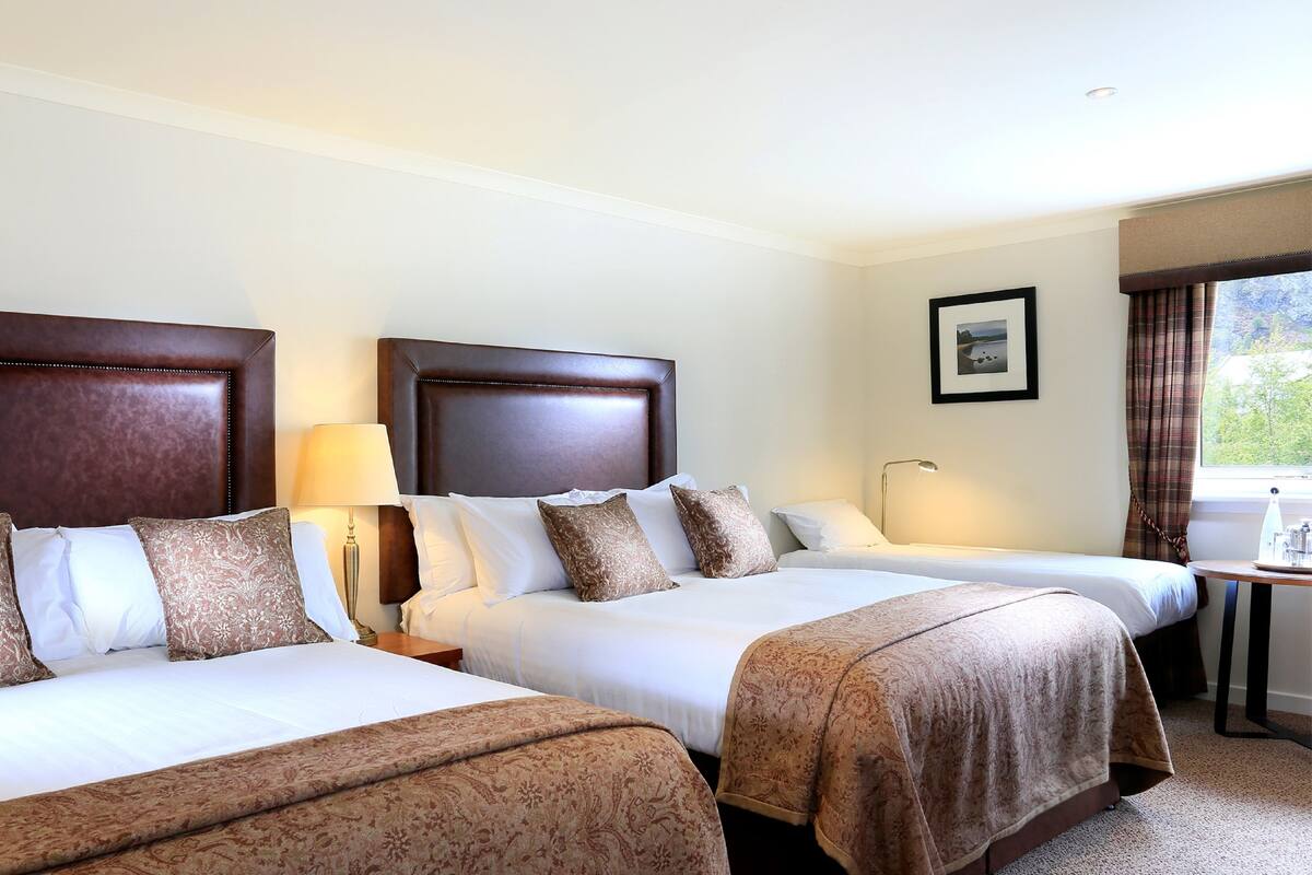A hotel room with two beds, a desk, and a window with curtains.