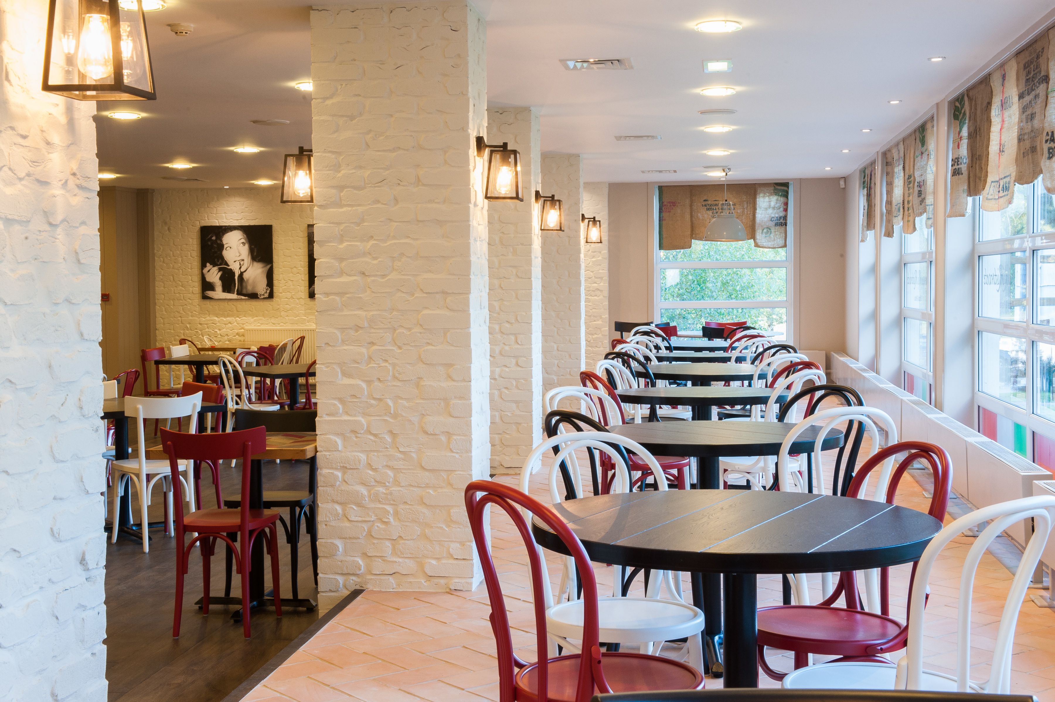 Un restaurant amb parets de maó, diverses taules i cadires, i lluminàries penjants.