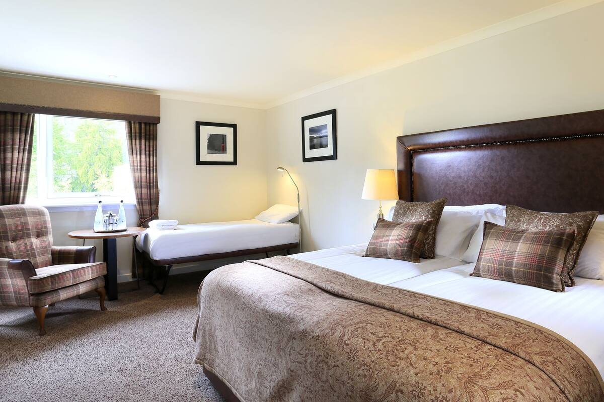A hotel room with two beds, a chair, a small table, and a window with curtains.
