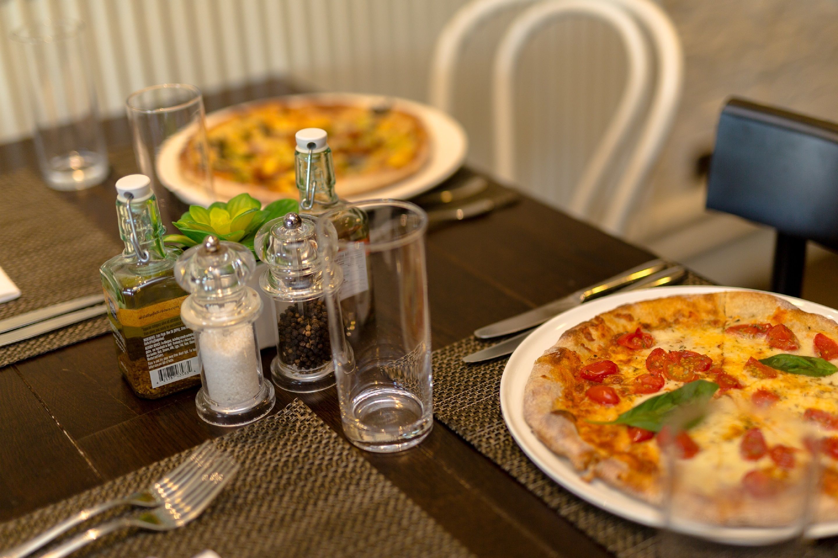 A dining table with a pizza, salt and pepper shakers, a bottle of olive oil, and a glass of water.