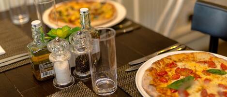A dining table with a pizza, salt and pepper shakers, a bottle of olive oil, and a glass of water.