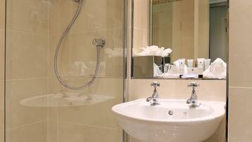 A modern bathroom with a glass-enclosed shower, a white sink, and a mirror reflecting toiletries.