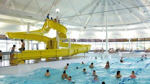 Ein Hallenbad mit gelber Rutsche und mehreren Schwimmbahnen.