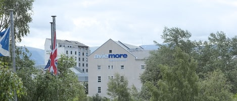 Un patio de hotel con mesas al aire libre, un asta de bandera y un edificio con letreros que dicen 'avie more'.