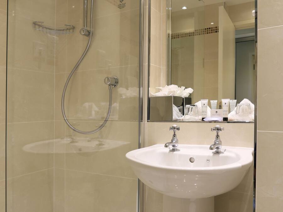 A modern bathroom with a glass-enclosed shower, a pedestal sink, and a tiled shower area.