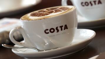A white cup with "COSTA" and "Italian about coffee" text, a spoon, and a saucer on a table.