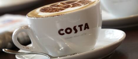 A white cup with "COSTA" and "Italian about coffee" text, a spoon, and a saucer on a table.
