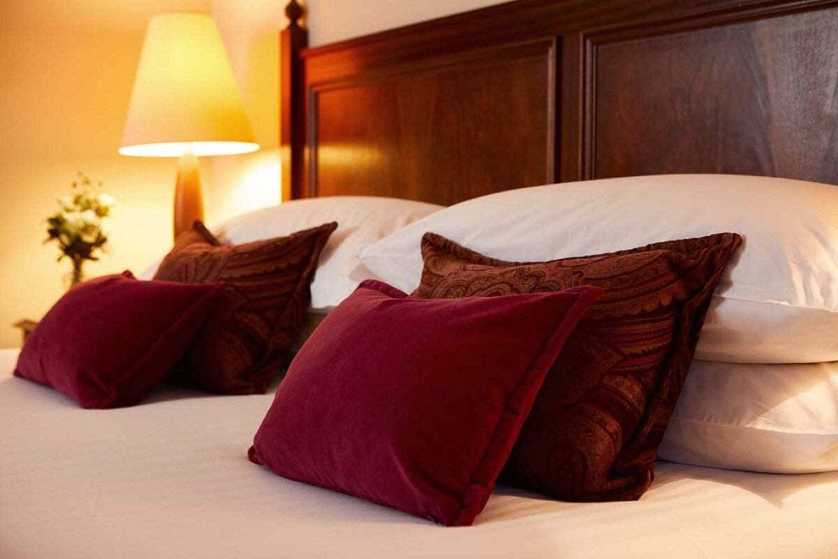 Une chambre d’hôtel avec une tête de lit en bois, deux oreillers blancs et deux oreillers rouges.