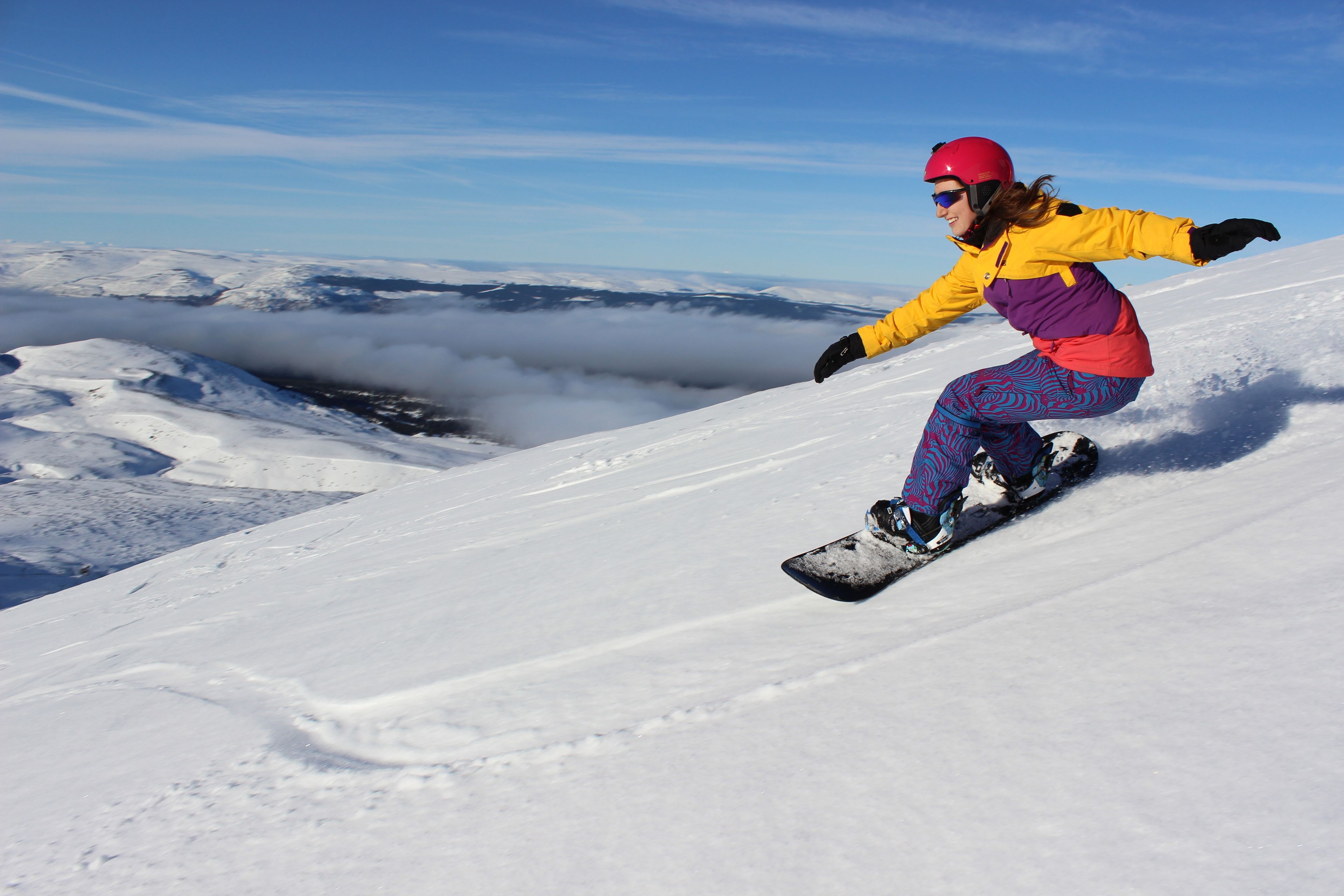 Un snowboardeur sur une pente enneigée, avec un ciel dégagé et des nuages en arrière-plan.