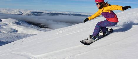 Un snowboardeur sur une pente enneigée, avec un ciel dégagé et des nuages en arrière-plan.
