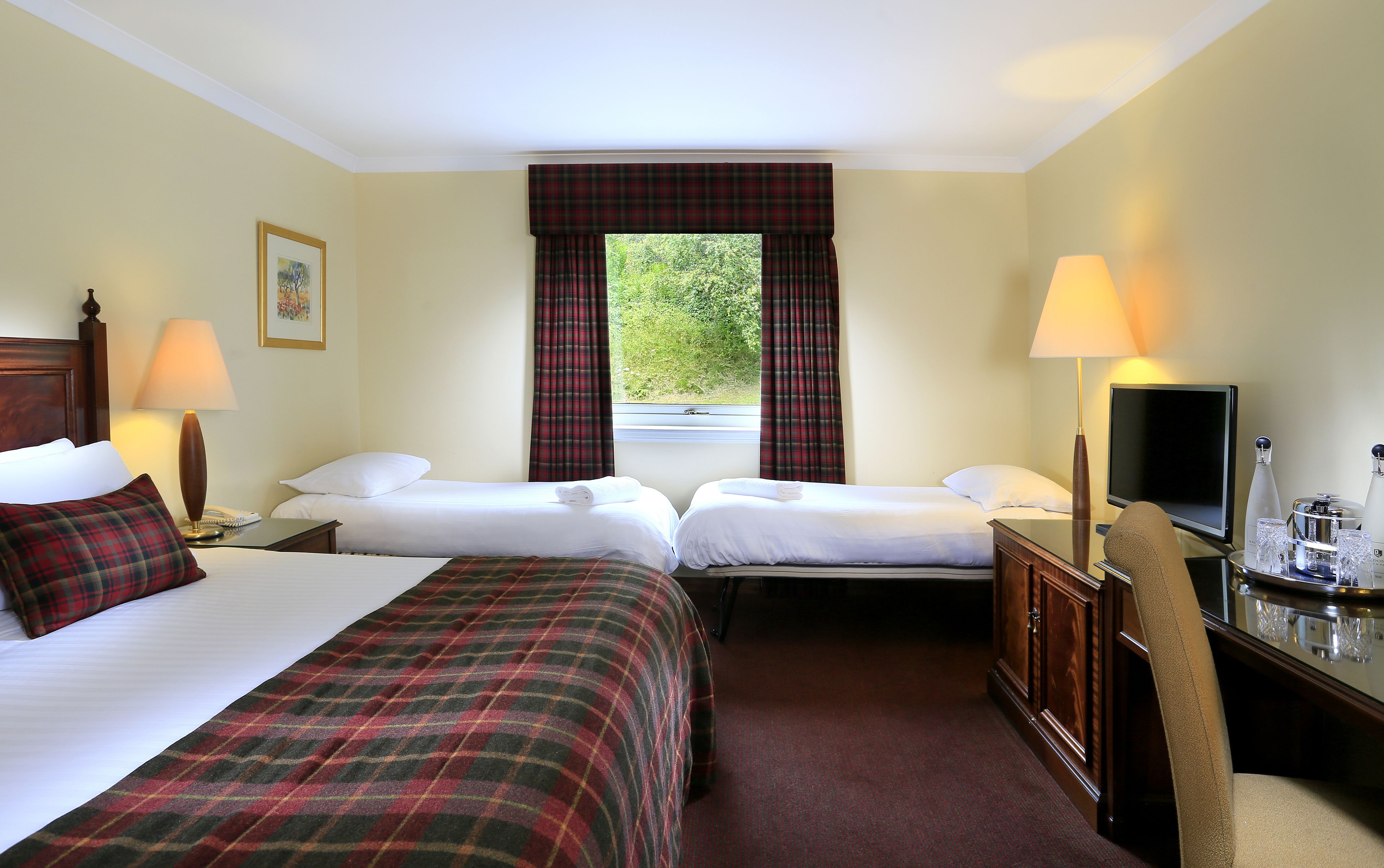 A hotel room with two beds, a television, a desk with a lamp, and a window with curtains.