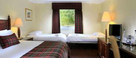 A hotel room with two beds, a television, a desk with a lamp, and a window with curtains.
