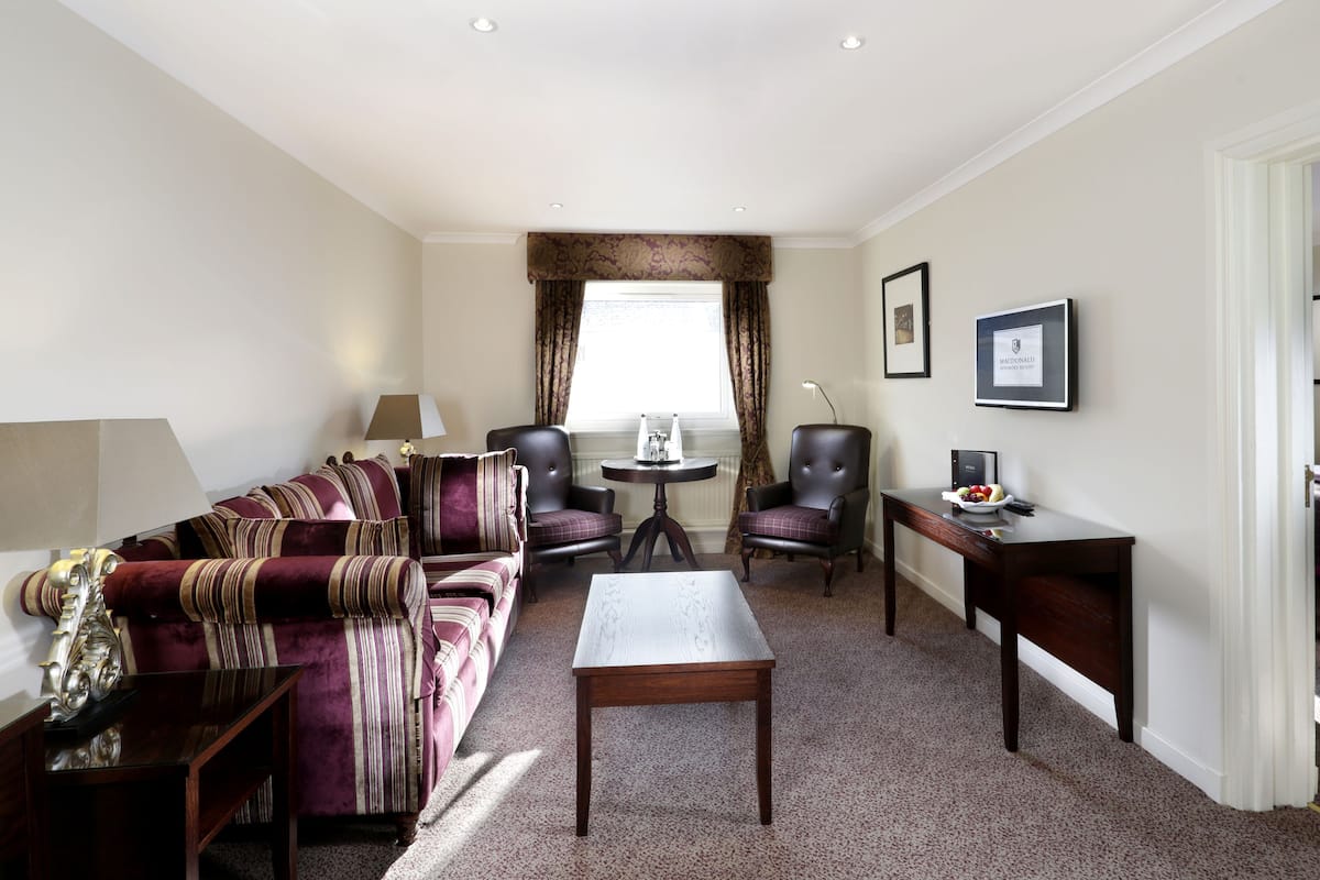 Habitación de hotel con sofá, dos sillones, una mesita, un escritorio y una cama.