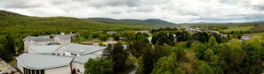 Un grand bâtiment doté de plusieurs toits, entouré d’une forêt verdoyante et dense, avec des collines en arrière-plan.