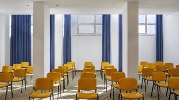 A conference room with rows of yellow chairs and blue curtains, large windows, and a patterned floor.