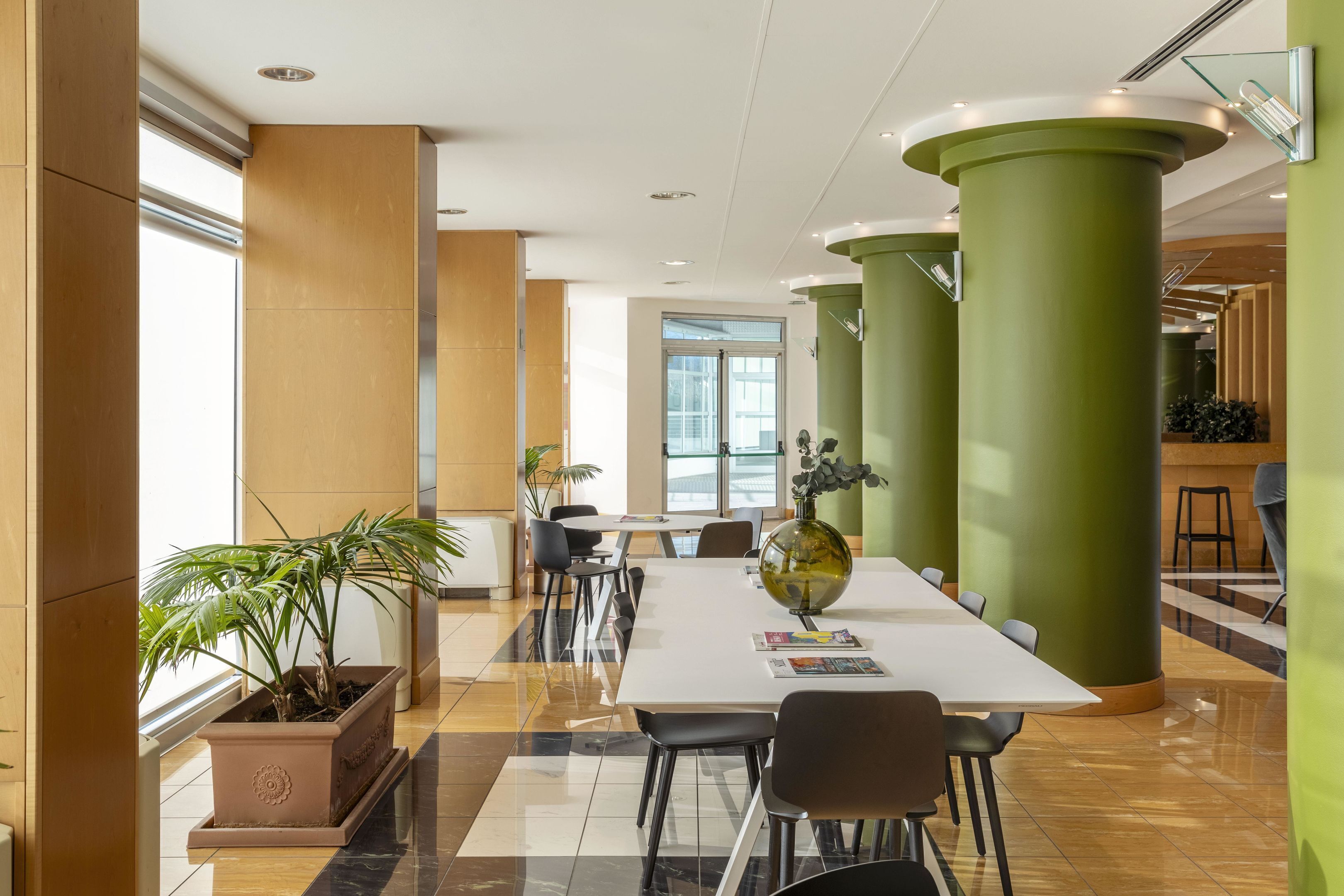 Een moderne vergaderruimte met een witte tafel, zwarte stoelen en groene zuilen.