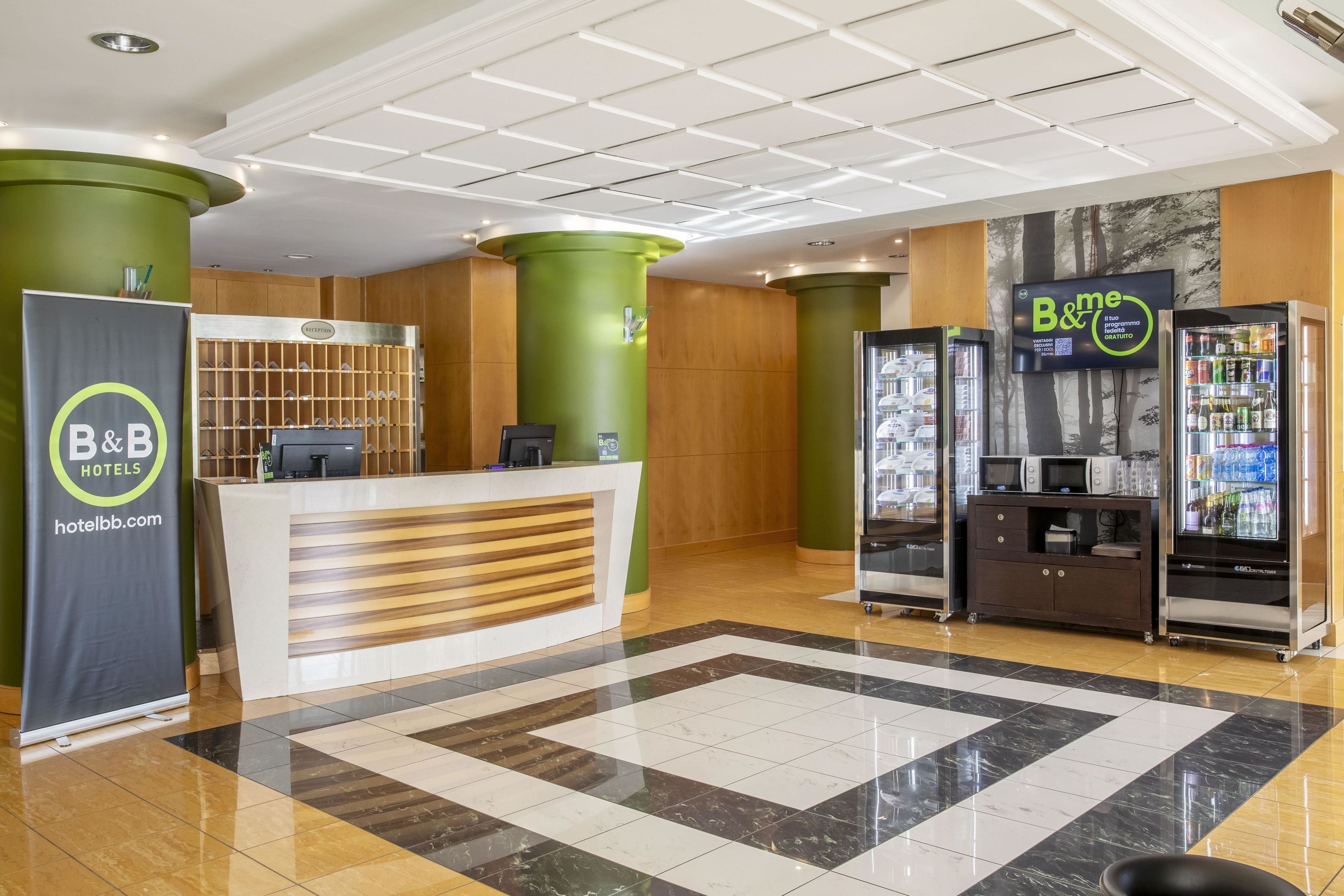 A hotel reception area with a reception desk, a B&B sign, a digital screen, and vending machines.