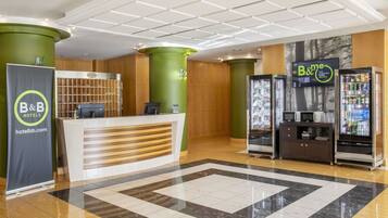 A hotel reception area with a reception desk, a B&B sign, a digital screen, and vending machines.