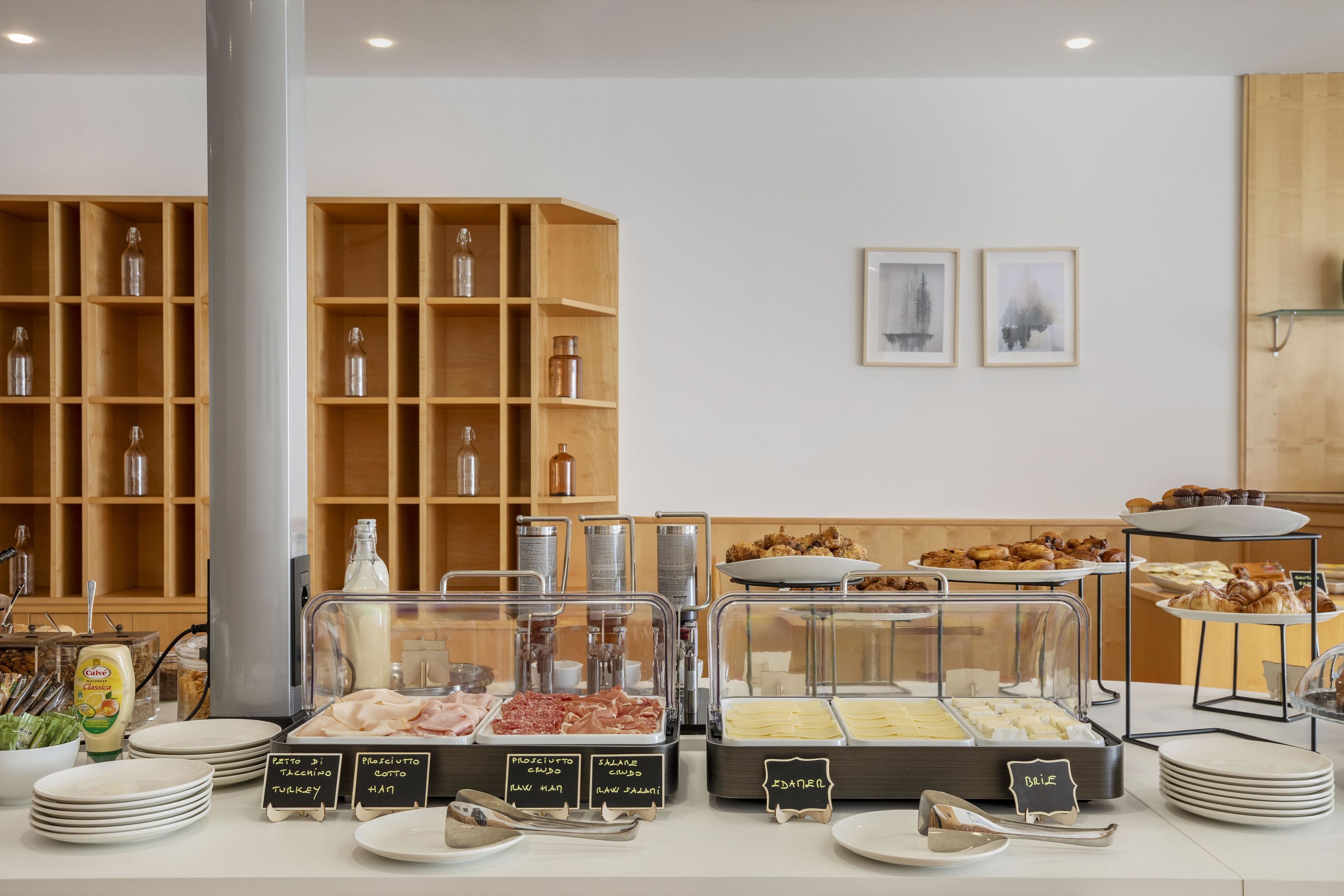 Uma área de buffet com diversas opções de comida, incluindo carnes e queijos, e uma variedade de produtos de panificação.