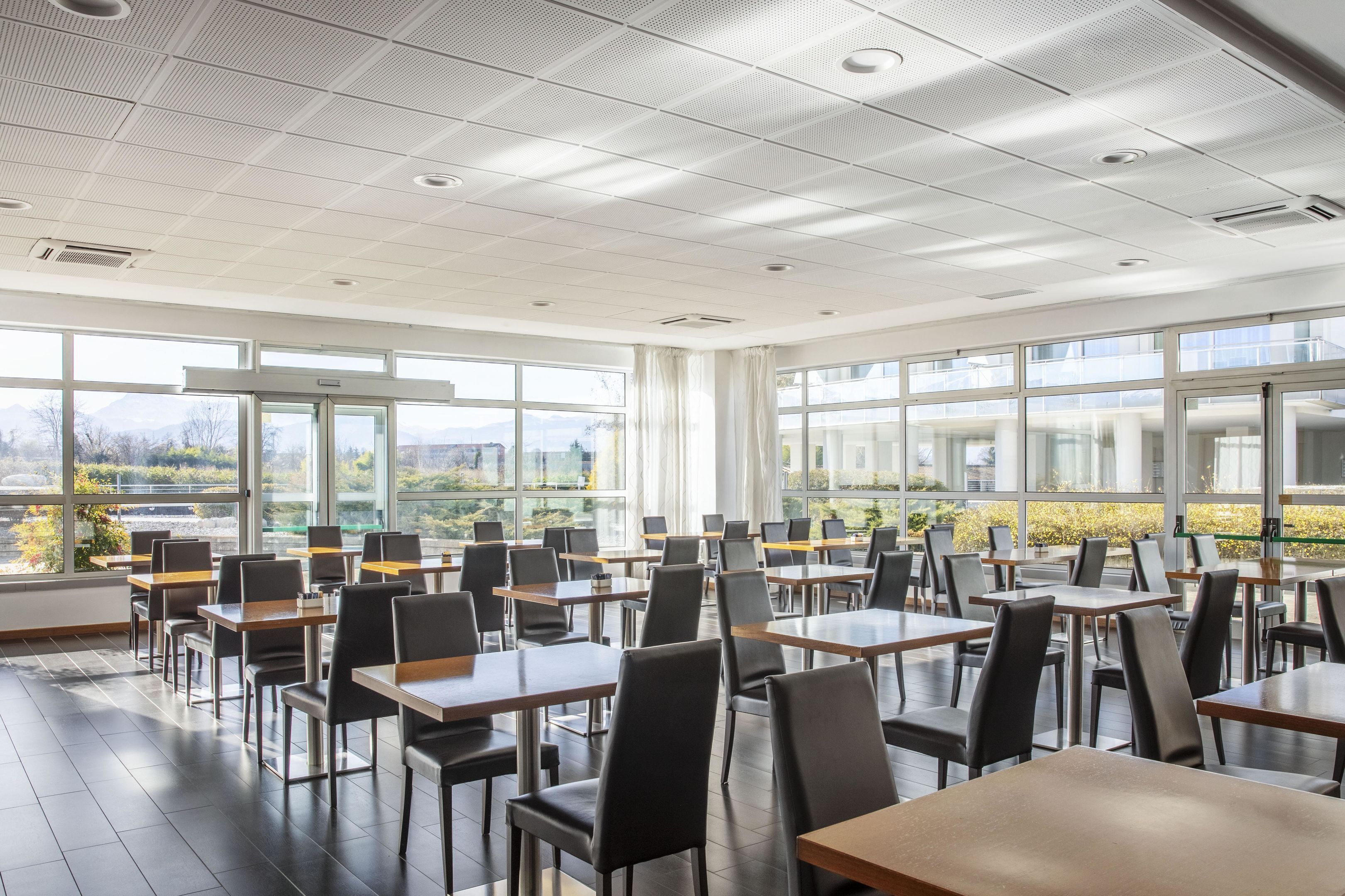 Un comedor amplio con mesas y sillas, ventanas grandes que ofrecen vistas al exterior e iluminación empotrada en el techo.