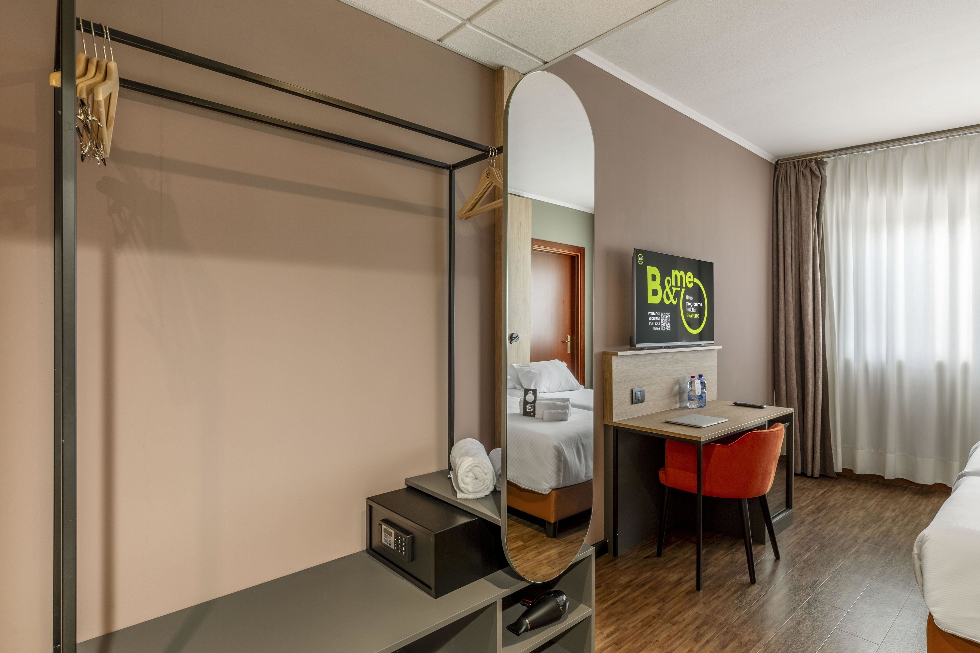 Ein Hotelzimmer mit Bett, Schreibtisch, Stuhl, Spiegel, Fernseher und einer Badezimmertür.