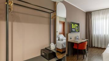 Ein Hotelzimmer mit Bett, Schreibtisch, Stuhl, Spiegel, Fernseher und einer Badezimmertür.