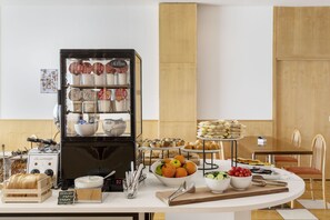 Un bufé de desayuno con diferentes alimentos, una máquina de café y un letrero que indica opciones de yogur y queso.
