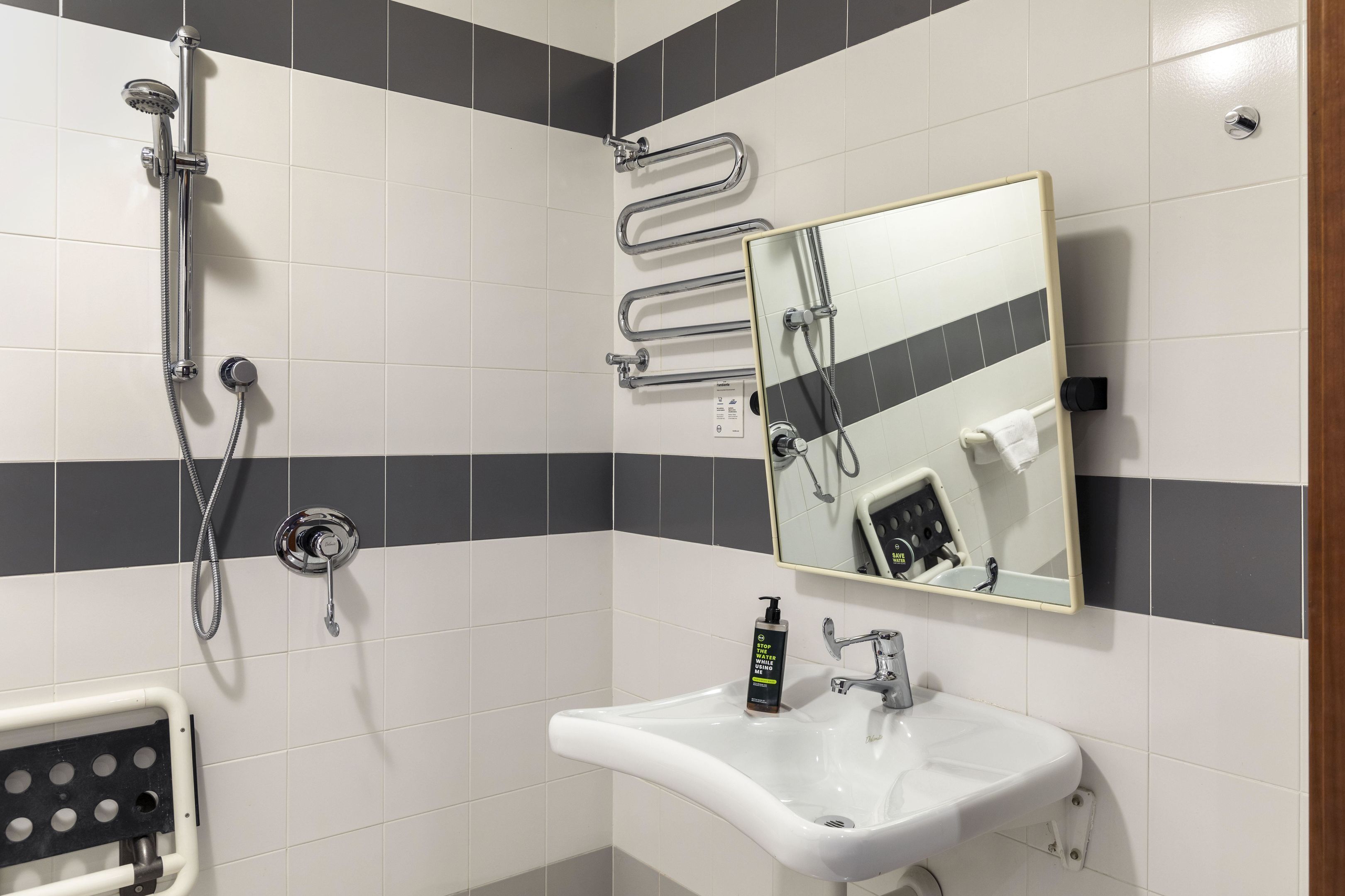 Une salle de bain équipée d’une douche, d’un lavabo, d’un miroir et d’un distributeur de gel hydroalcoolique.