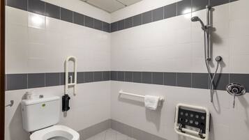 Un baño con inodoro, ducha y barra de apoyo.