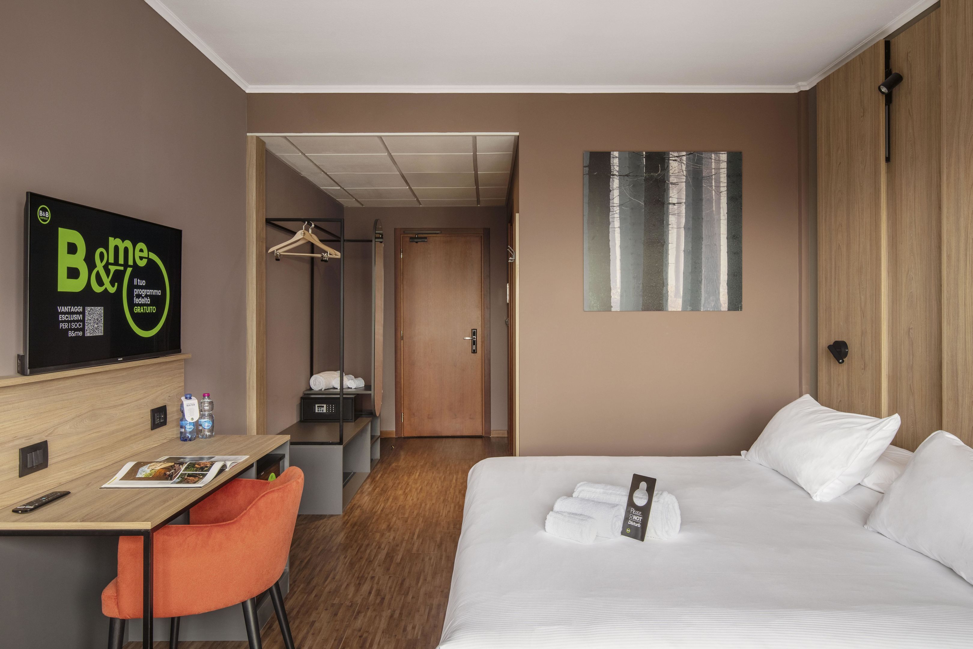 Une chambre d’hôtel comprenant un lit, un bureau avec une chaise, un porte-manteau et une armoire.