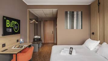Une chambre d’hôtel comprenant un lit, un bureau avec une chaise, un porte-manteau et une armoire.