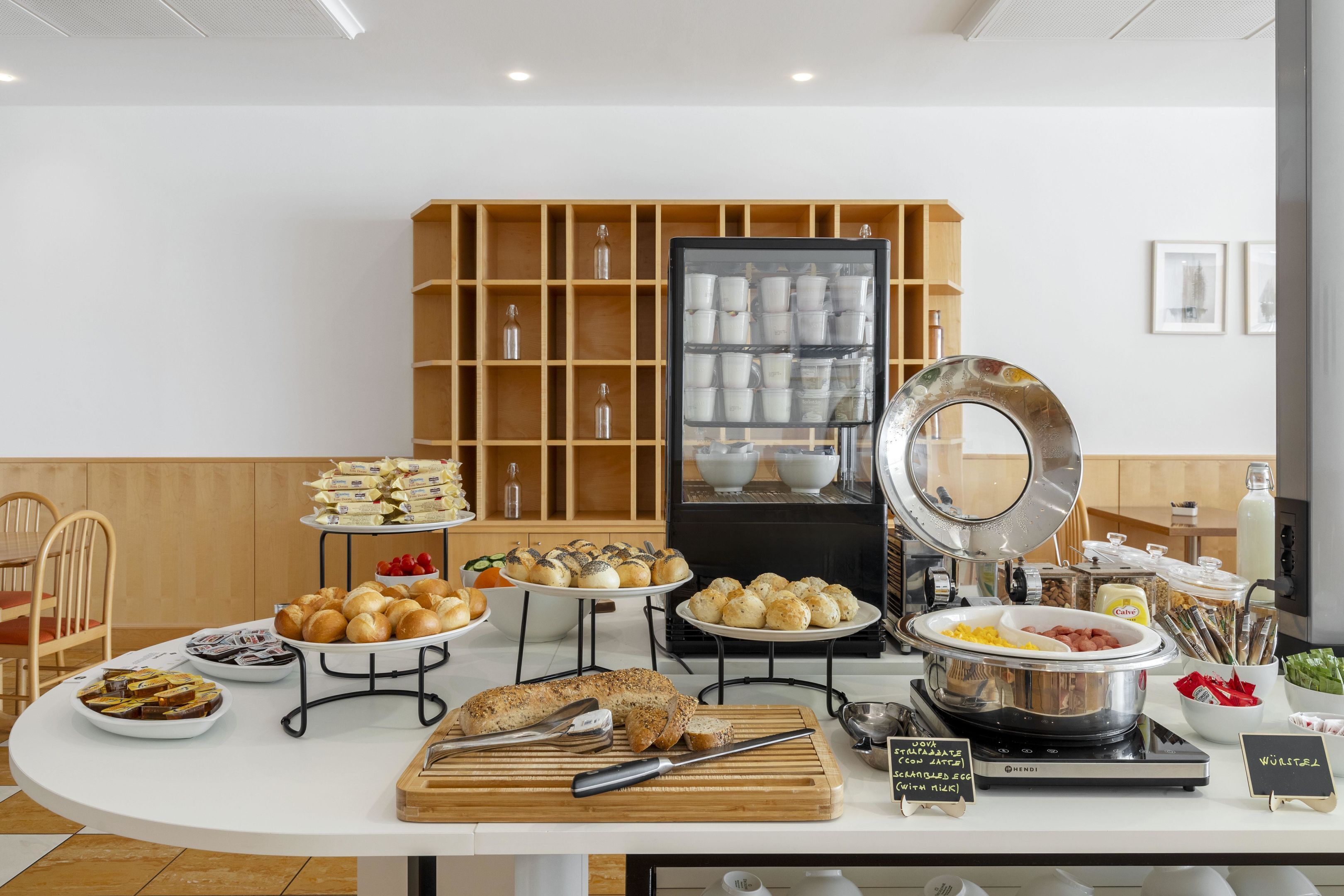 A buffet setup with various food items, a cutting board with utensils, and a sign indicating a vegetarian option.