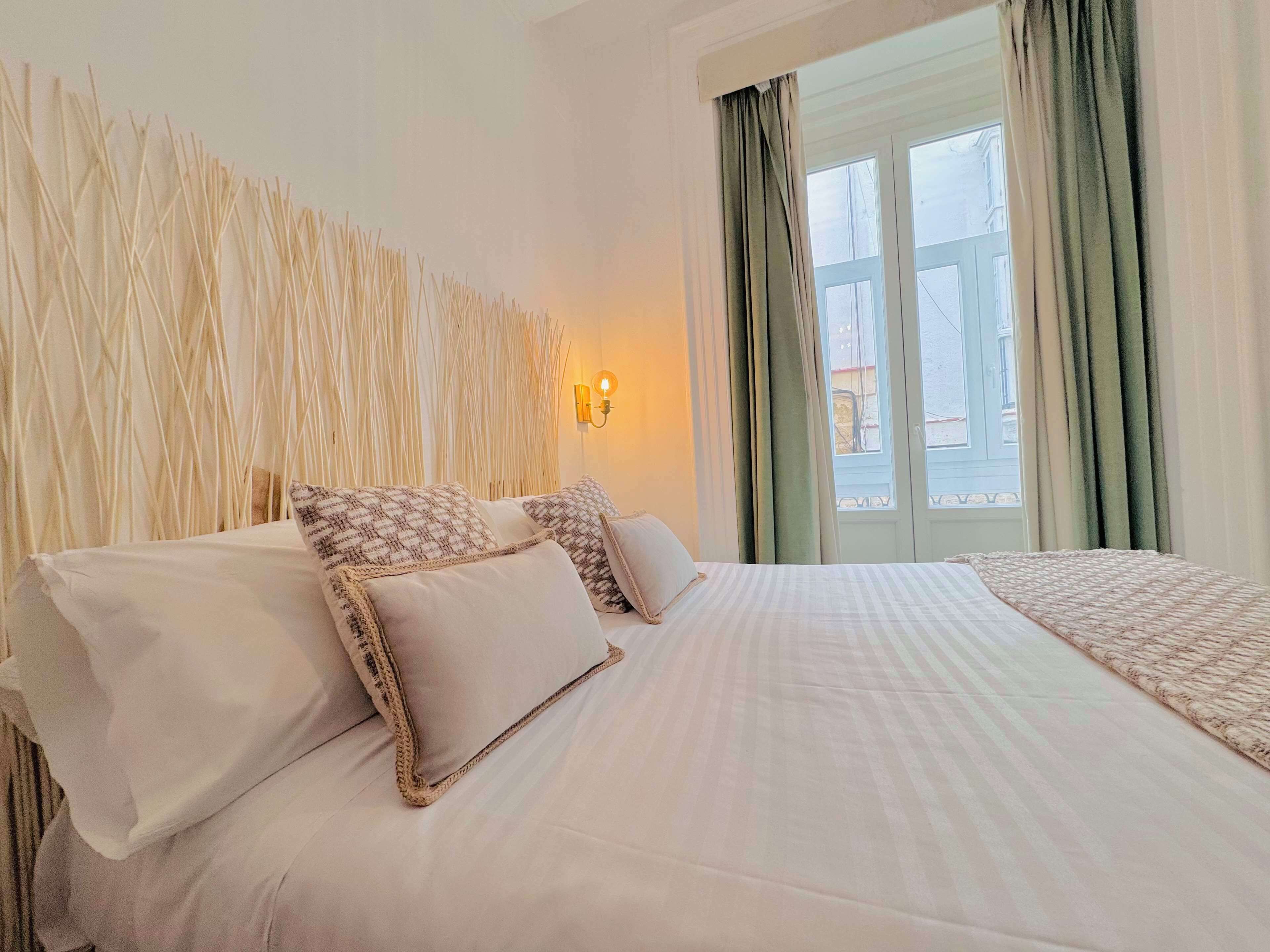 A hotel room with a bed, a wall-mounted light, and a window with curtains.