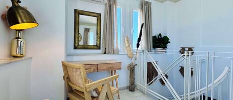 A modern room with a wooden desk, a lamp, a mirror, and a white railing.