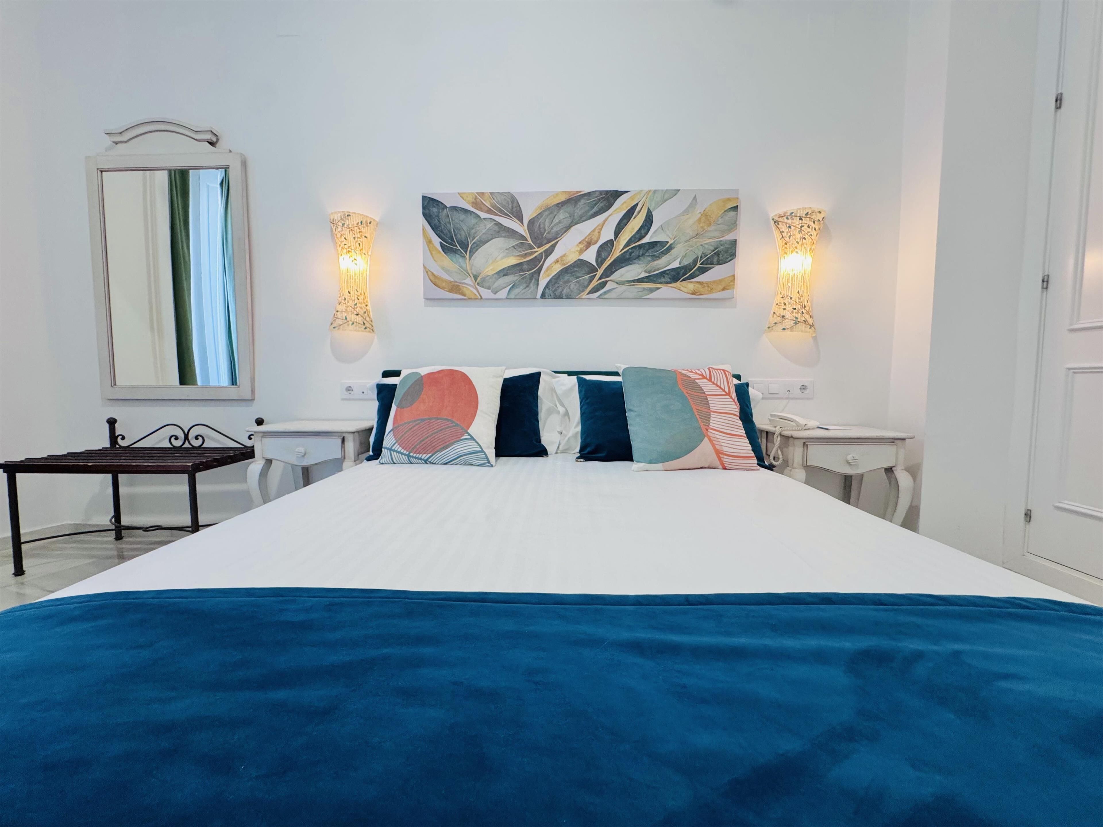 Ein Hotelzimmer mit einem großen Bett, zwei Nachttischen, einem kleinen Schreibtisch, einem Spiegel und Wandleuchten.