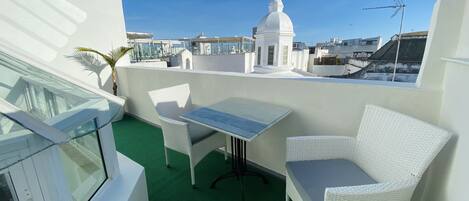 A rooftop terrace with a table and two white wicker chairs, a green artificial turf floor, and a white dome structure in the background.