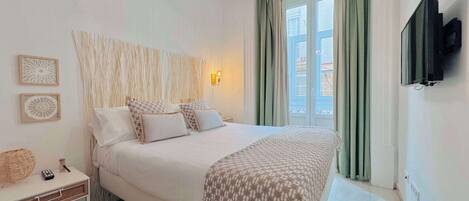 A bedroom with a bed, bedside table, lamp, and a TV mounted on the wall.