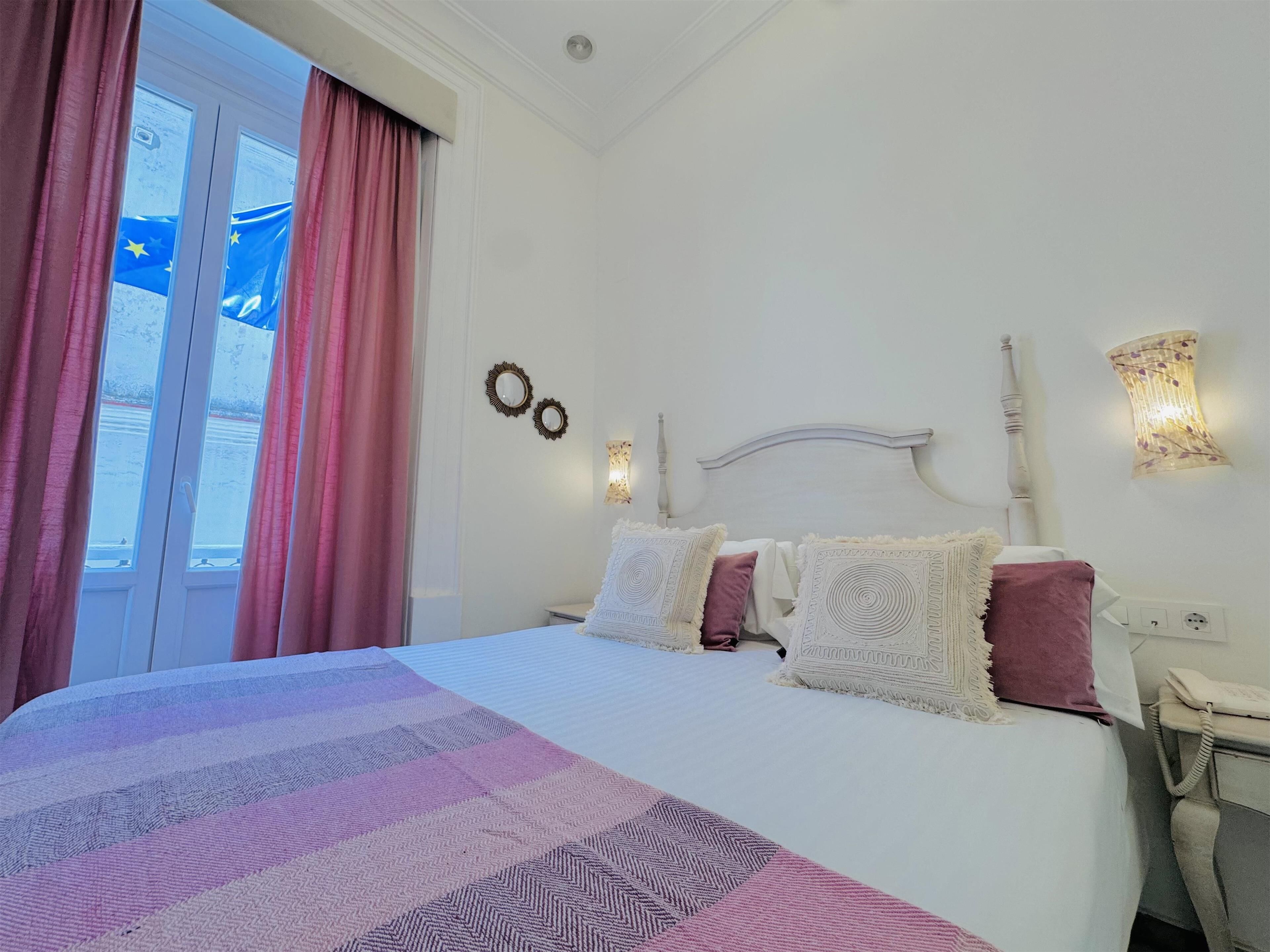 Ein Hotelzimmer mit Bett, Nachttisch, Lampe und Meerblick aus dem Fenster.