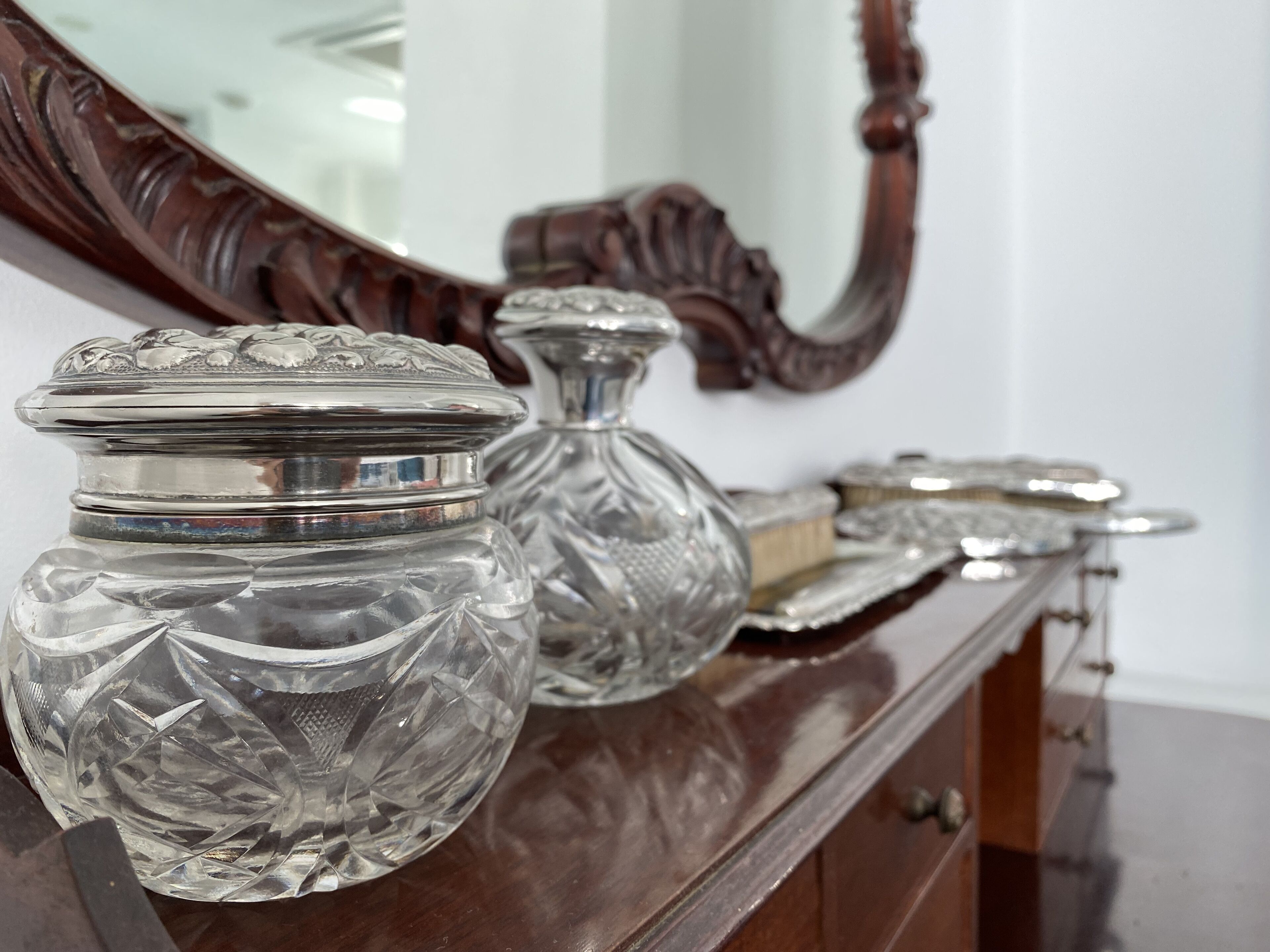 Une commode en bois, ornée de récipients en verre argenté et dotée d’un miroir.