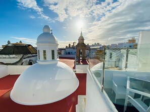 Una terraza en la azotea con una estructura abovedada blanca, una pequeña torre y barandilla de cristal.