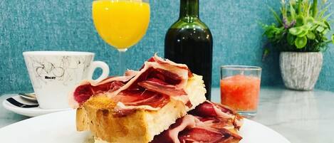 A breakfast plate with toast and ham, a glass of orange juice, a bottle of olive oil, a cup with a horse design, and a small potted plant.