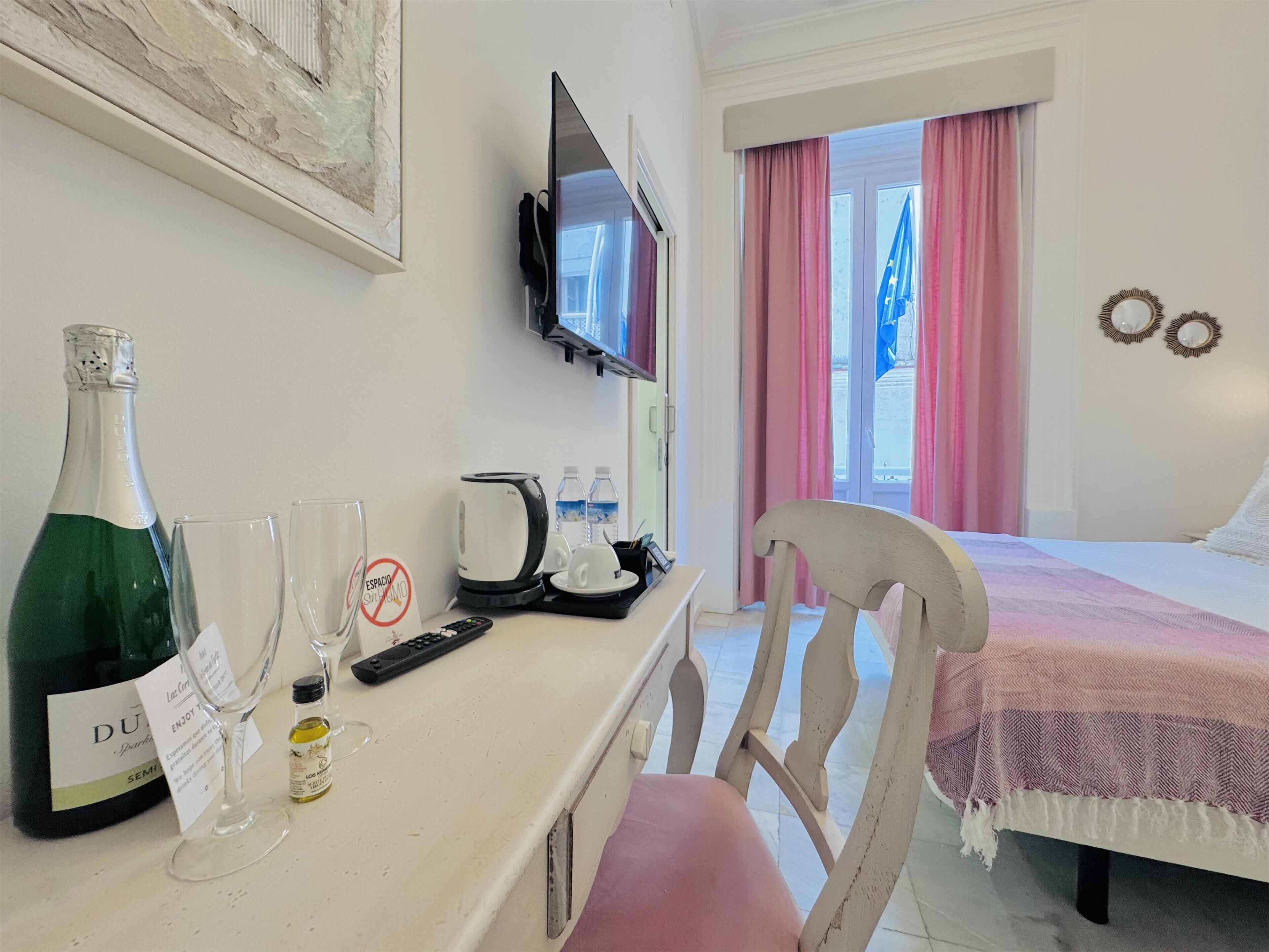 Ett hotellrum med en säng, ett skrivbord med en flaska champagne, glas, en vattenkokare och en fjärrkontroll.