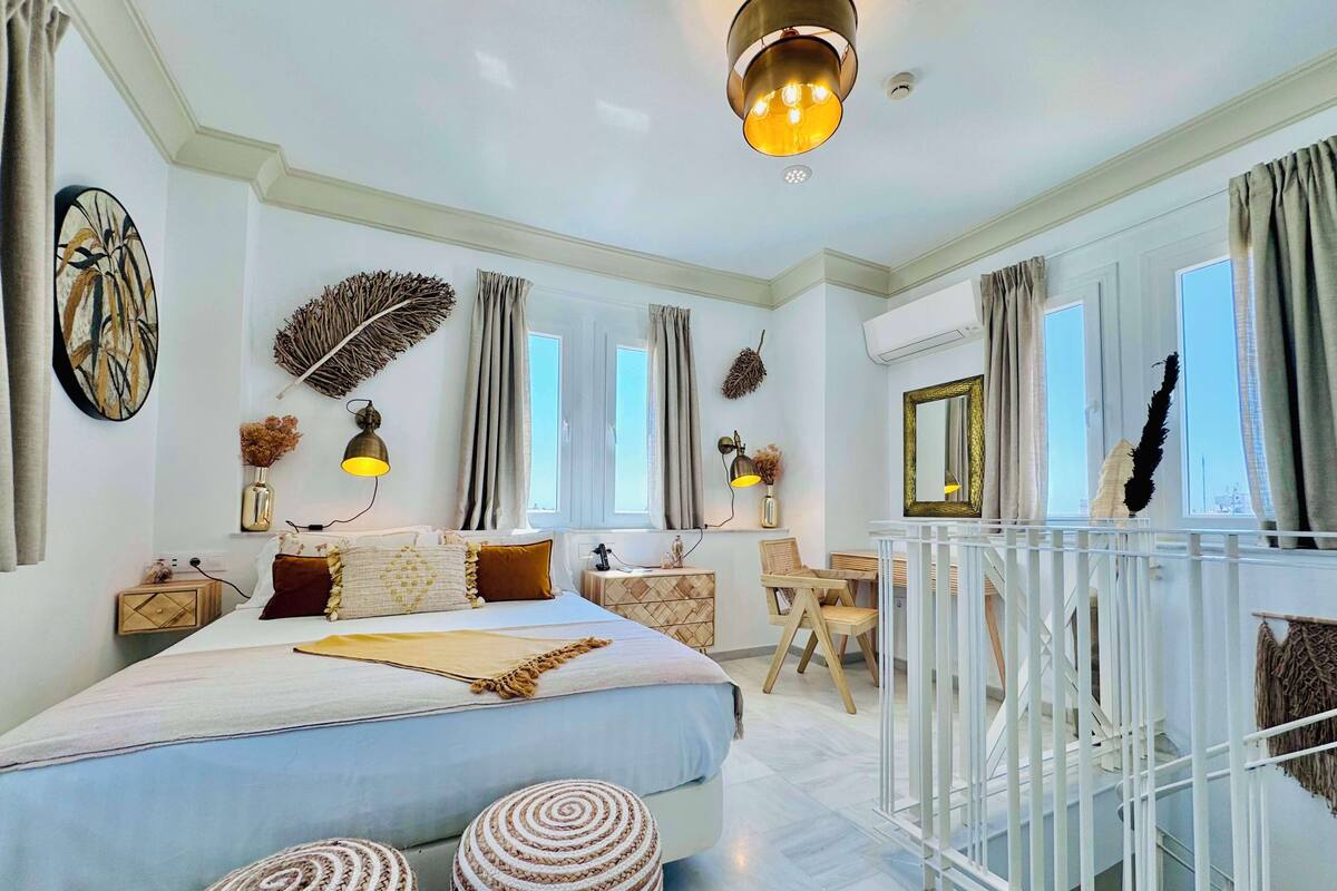 Een moderne slaapkamer met een groot bed, nachtkastjes, een bureau en een balkon met een balustrade.