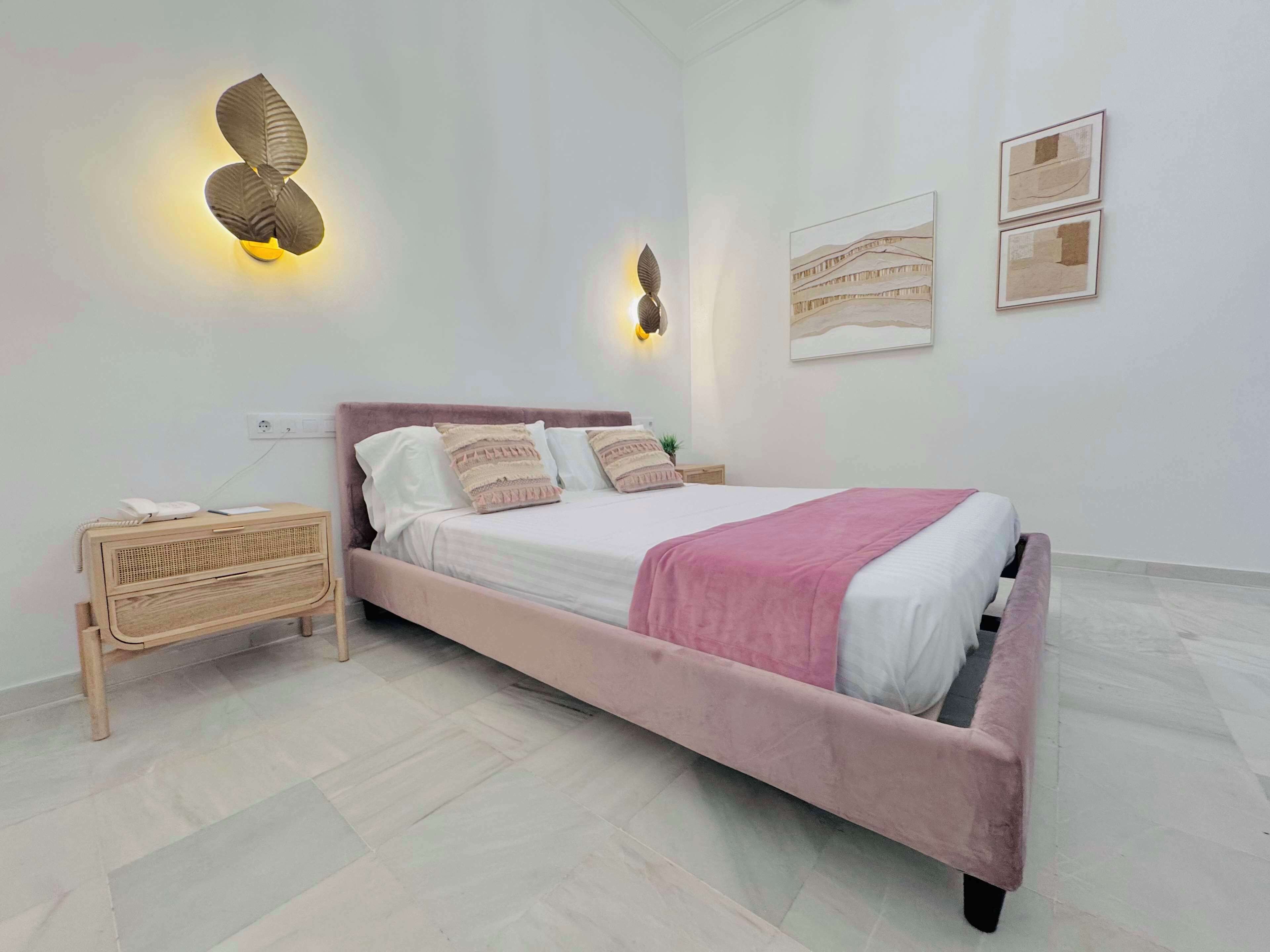 A modern bedroom with a pink bed, a bedside table with a lamp, and wall-mounted artwork.