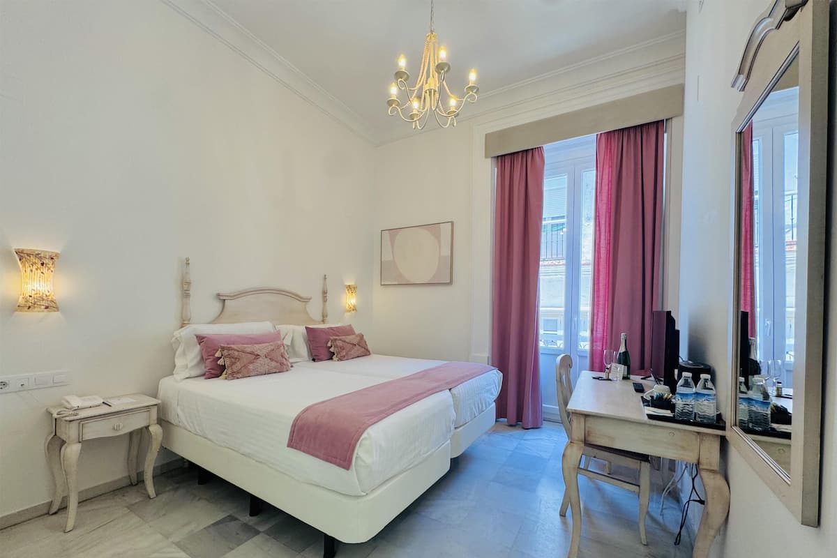 Een hotelkamer met een bed, nachtkastje, bureau, stoel en een groot raam met gordijnen.