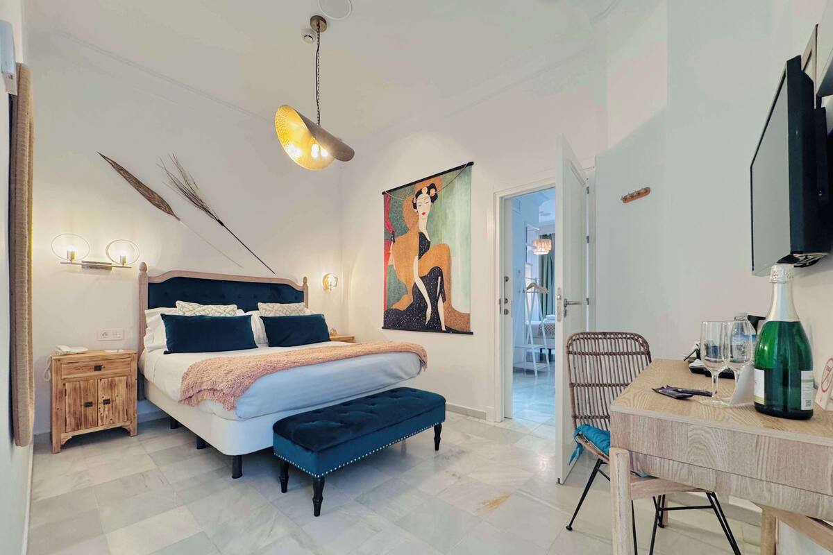 Een moderne slaapkamer met een groot bed, nachtkastjes, een bureau met stoel, een hanglamp en een schilderij aan de muur.