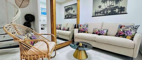 A living room with a large mirror, a wicker chair, a sofa with floral cushions, and a coffee table.